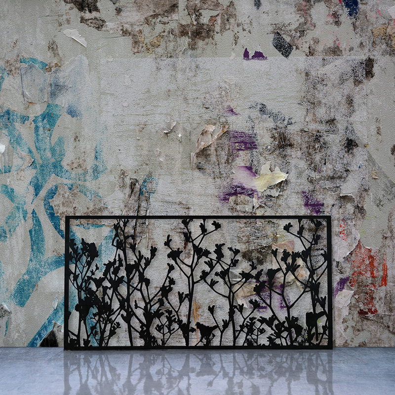 Laser Cut Black Metal Screen leaning on a factory wall with graffiti and street posters