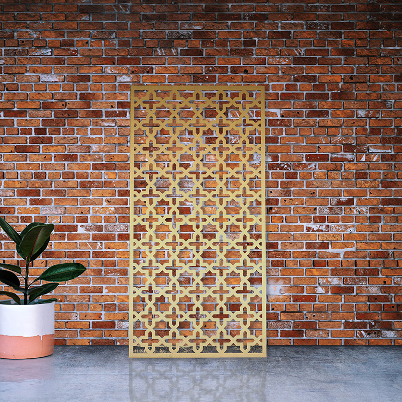 Gold Metal Garden screen with decorative laser cut design in brass leaning on factory wall