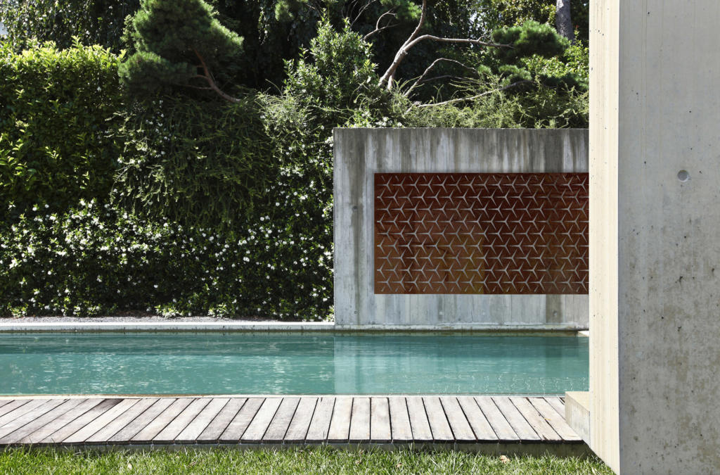 Laser cut screen made from Corten Steel hanging on concrete wall overlooking pool in modern landscape