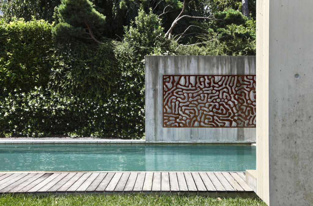Decorative Screen hanging as metal wall art over pool in modern landscape