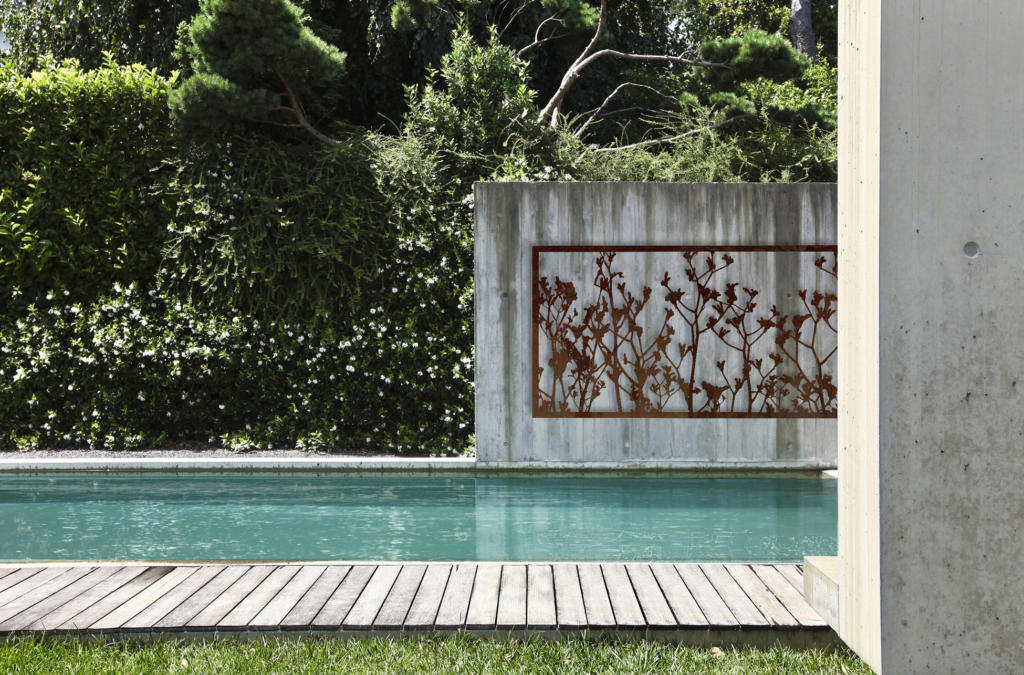 Laser cut screen by Lump Sculpture Studio hanging on concrete wall over modern pool