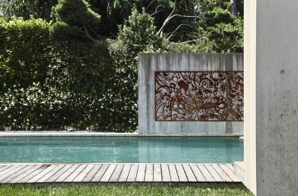 Decorative Screen made from corten steel with natural rusted finish hanging on concrete wall over pool in modern landscape