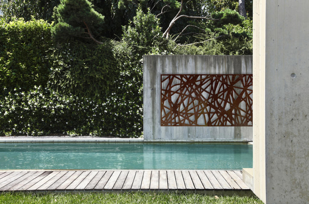Metal laser cut Screen hanging on concrete wall over modern pool landscape