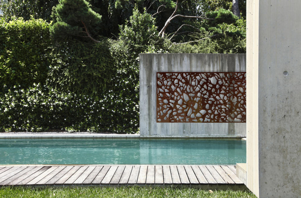 Metal laser cut Screen hanging on concrete wall over modern pool landscape