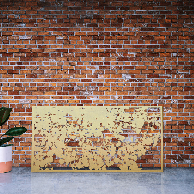 Gold Metal Garden screen with decorative laser cut design in brass leaning on factory wall