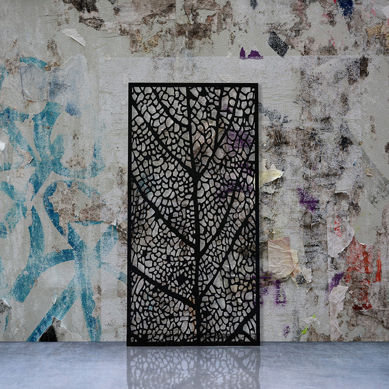 Black metal garden screen with laser cut screen design leaning on factory wall