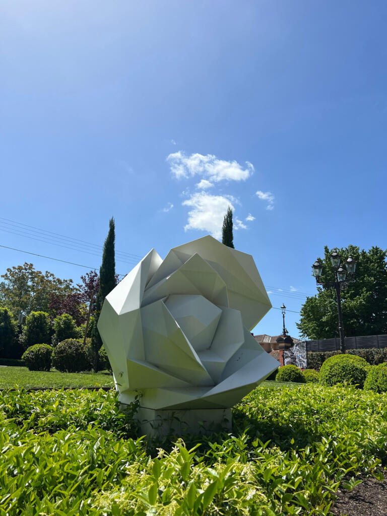 White Faceted Rose Sculpture by Lump Sculpture Studio displayed in a residential garden;