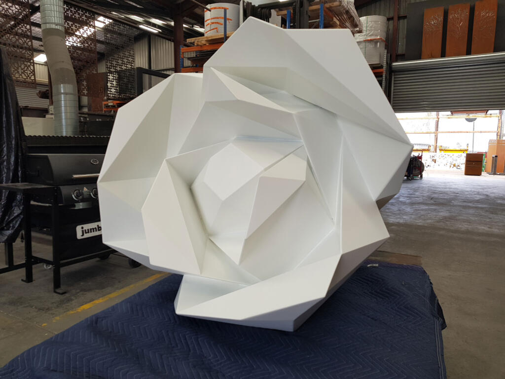 White Faceted Rose Sculpture by Lump Sculpture Studio displayed in a residential garden;