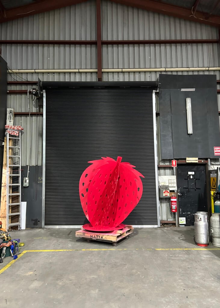 Large red strawberry sculpture at Yarra Farm Fresh, created by Lump Sculpture Studio, serving as a photo landmark for visitors.
