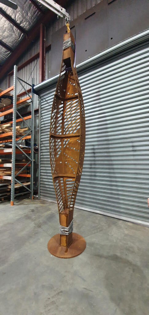 Corten steel and stainless steel canoe sculpture by First Nations artist Simone Thomson, fabricated by Lump Studio, installed on natural rock in Port Melbourne.