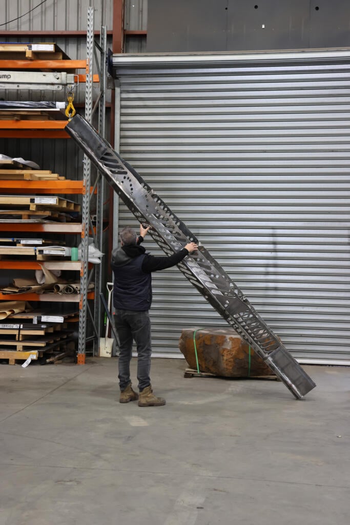 Corten steel and stainless steel canoe sculpture by First Nations artist Simone Thomson, fabricated by Lump Studio, installed on natural rock in Port Melbourne.
